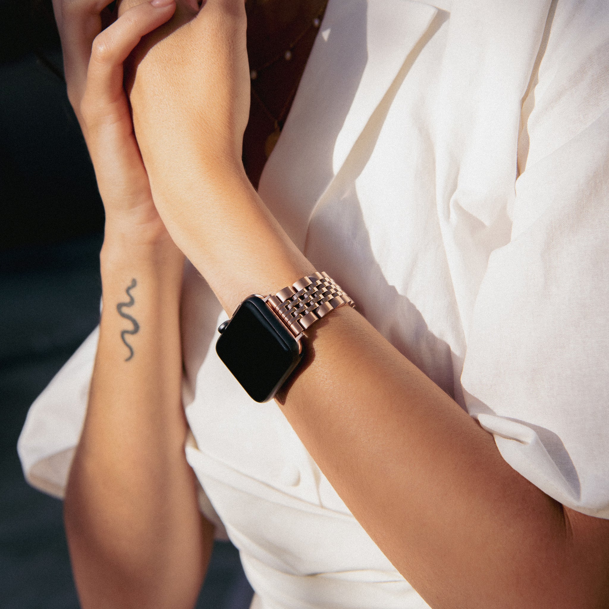 Person wearing a smartwatch with a metallic band and a snake tattoo on their arm.